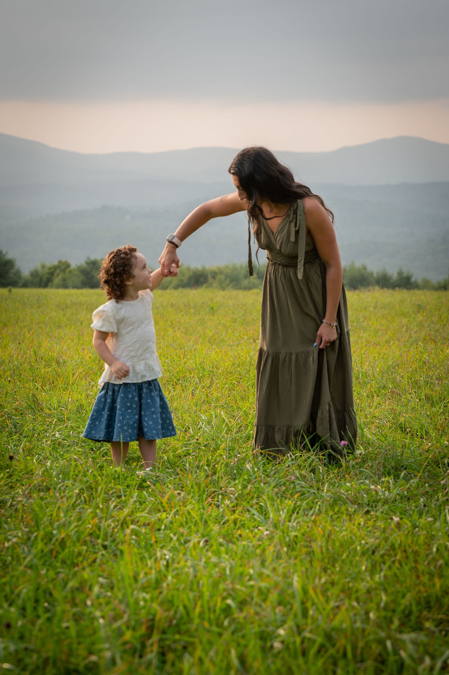A parent and child share a tender moment in a mountain meadow with rolling hills in the background. New Hampshire Family photographer