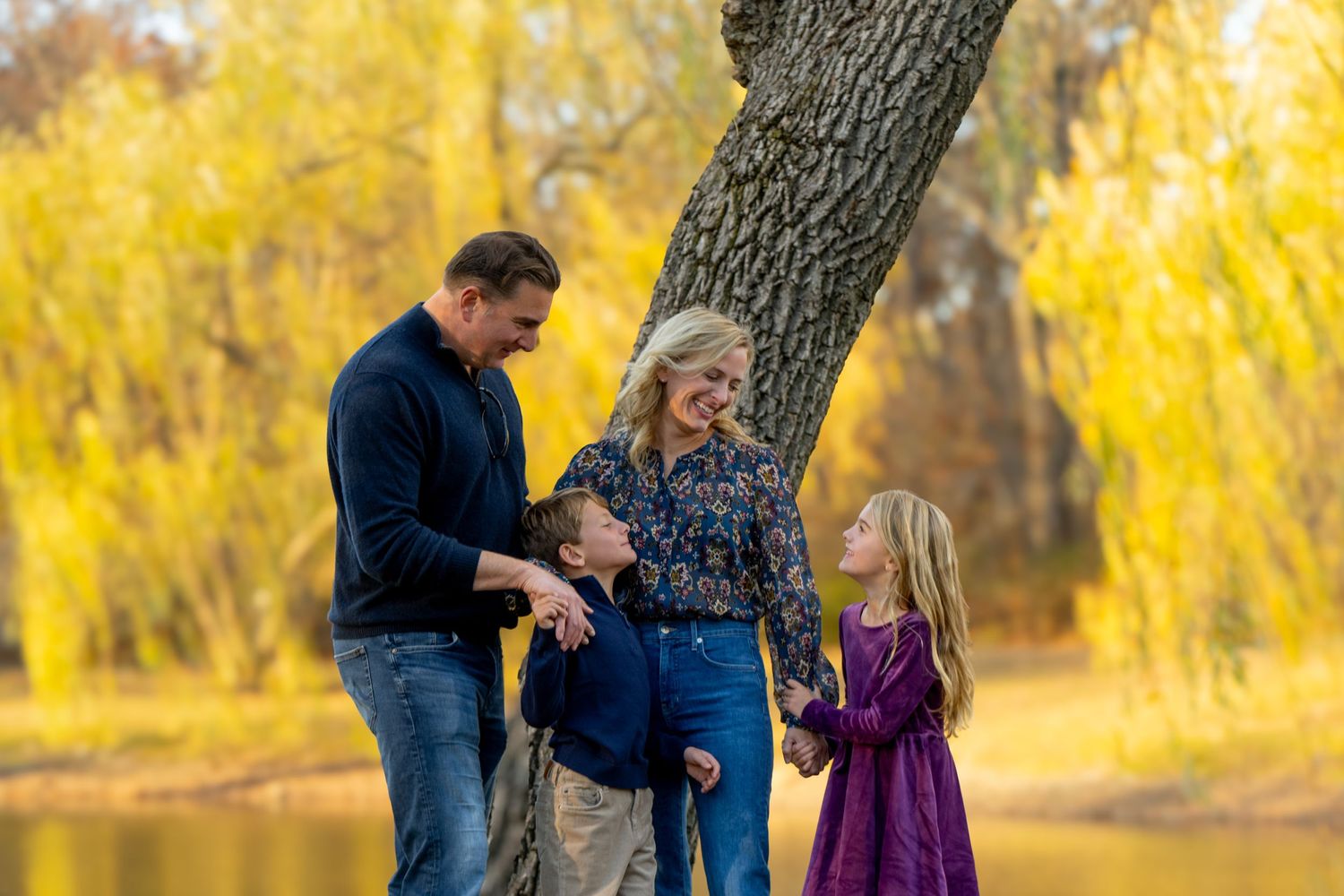 A family enjoys an autumn day near a lake with golden willows in the background providing a warm seasonal atmosphere.
