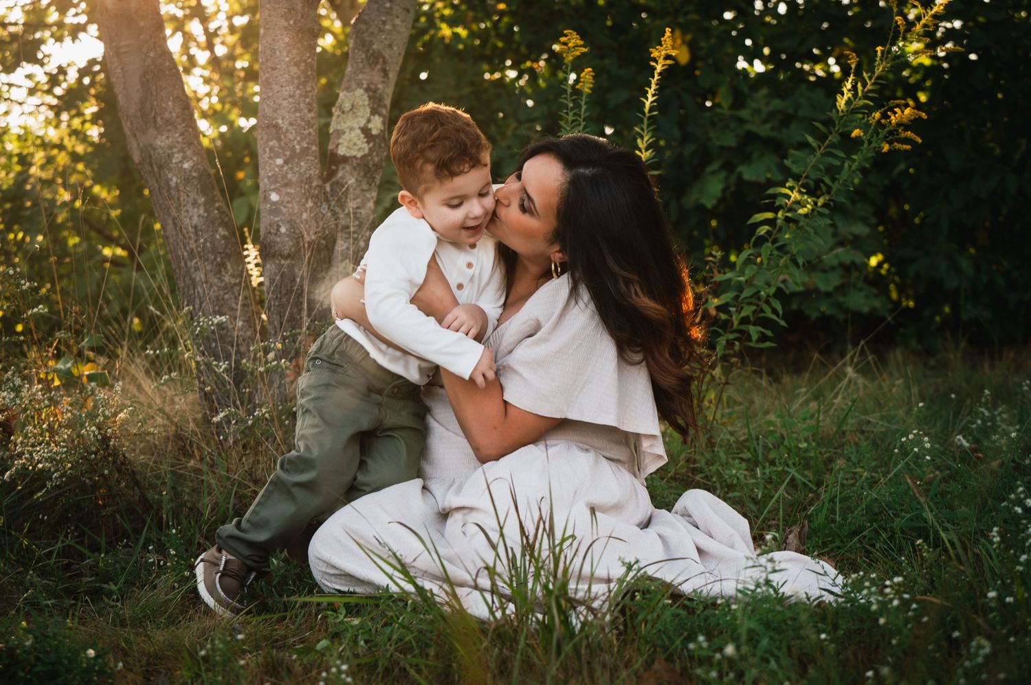 A tender moment between parent and child sitting in golden sunlit grass .Massachusetts Family photographer Serving New England Affordable
