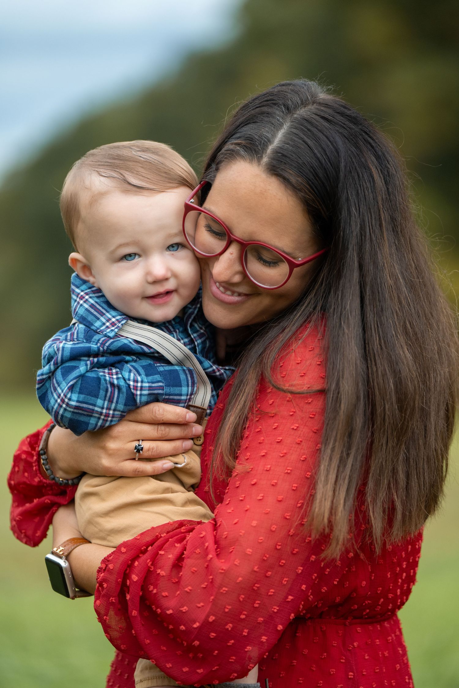 A tender moment captured between parent and baby in matching red and blue outfits outdoors. Massachusetts Family photographer