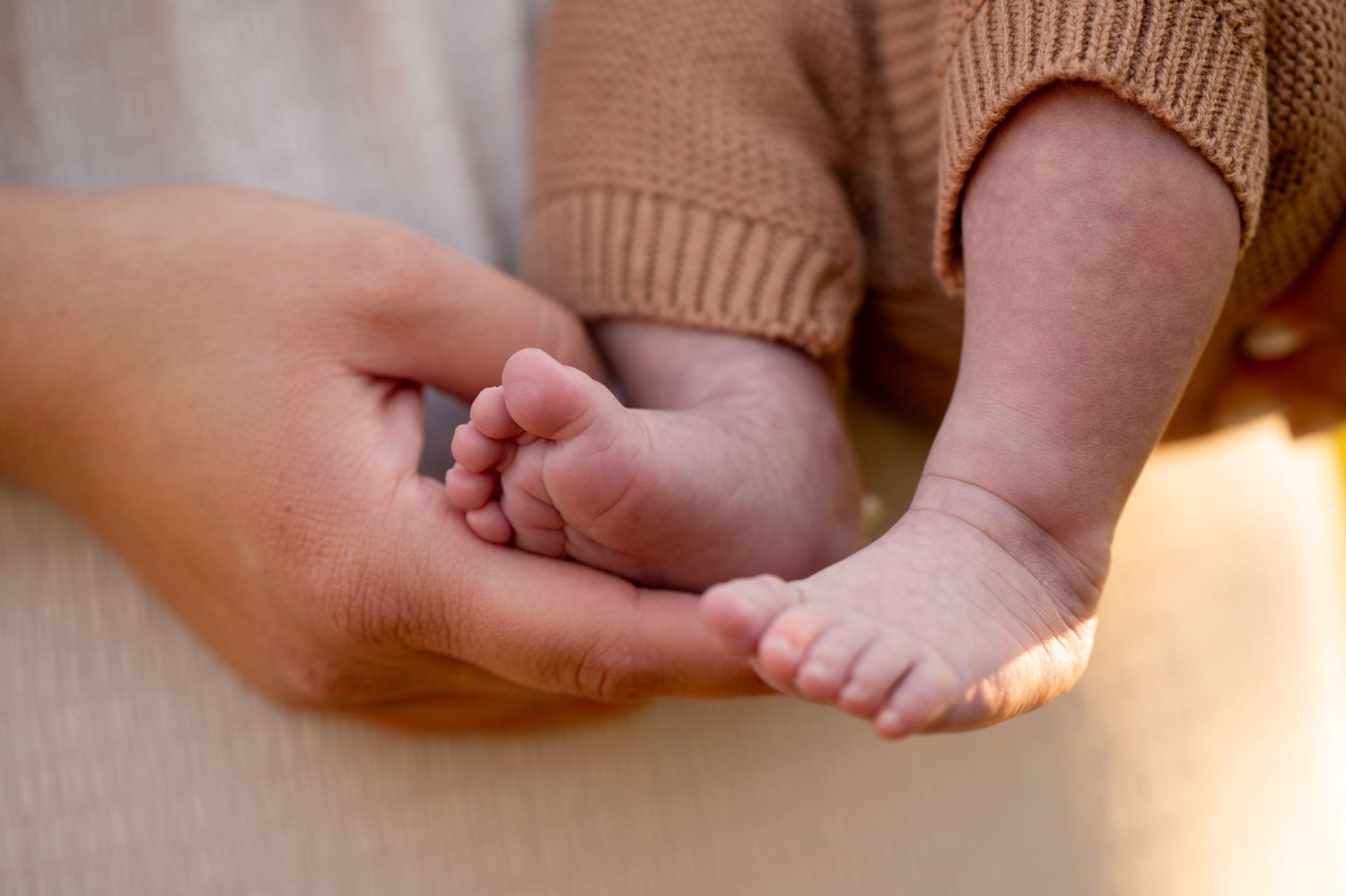 A tiny baby foot rests gently in an adult's caring hand, illuminated by warm sunlight. Massachusetts Family Photographer Serving New England