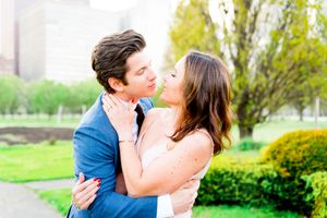 Man and woman in navy and pink hug and almost kiss in the middle of Chicago's Grant Park for sunset engagement pictures