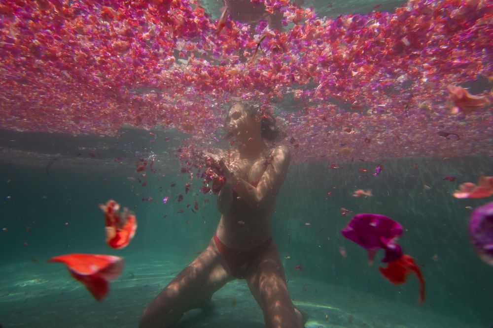 A girl kneeling underwater surrounded by flowers