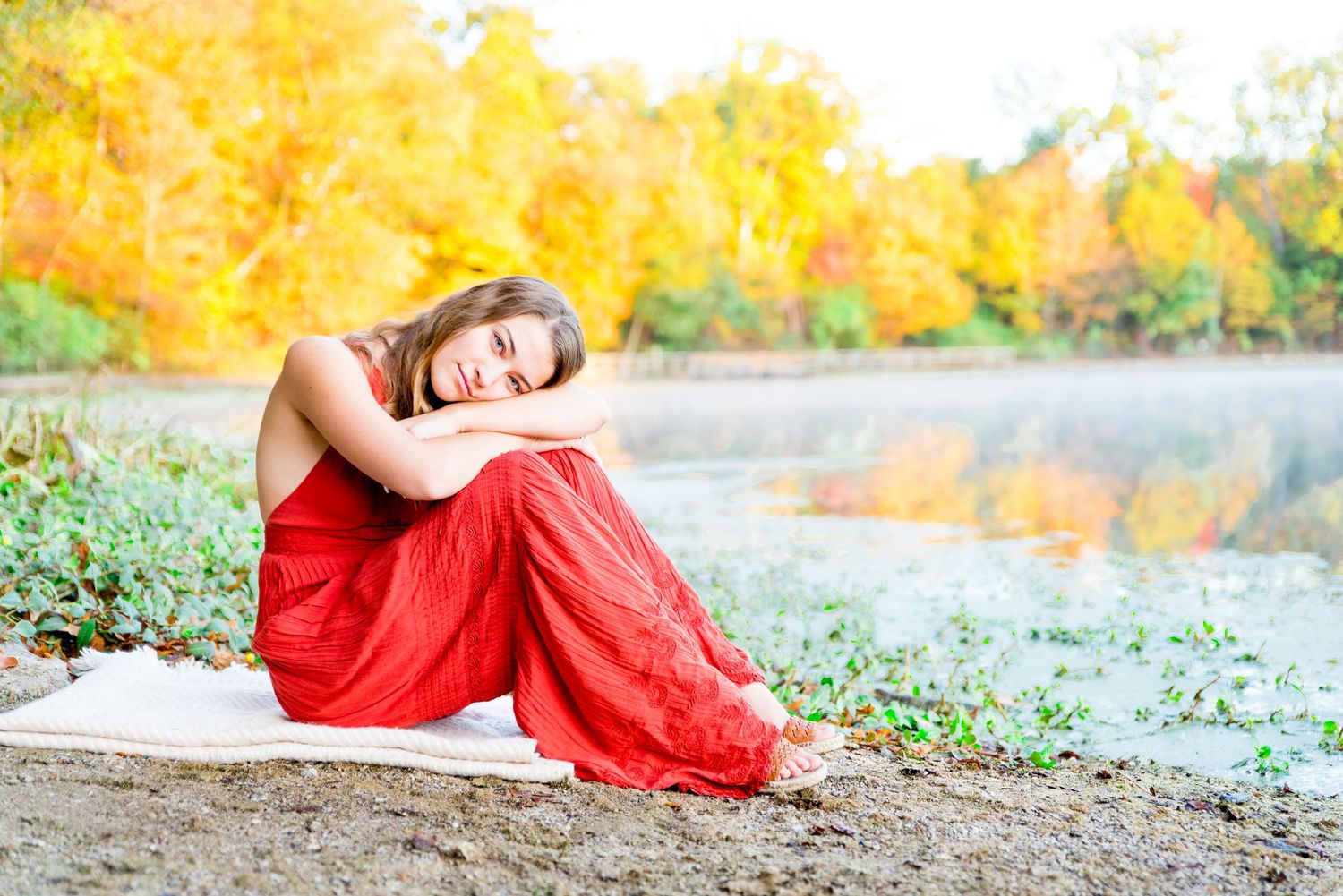 High school girl wearing orange jumpsuit sitting at the edge of a foggy pond in Chicago park leaning on her knees