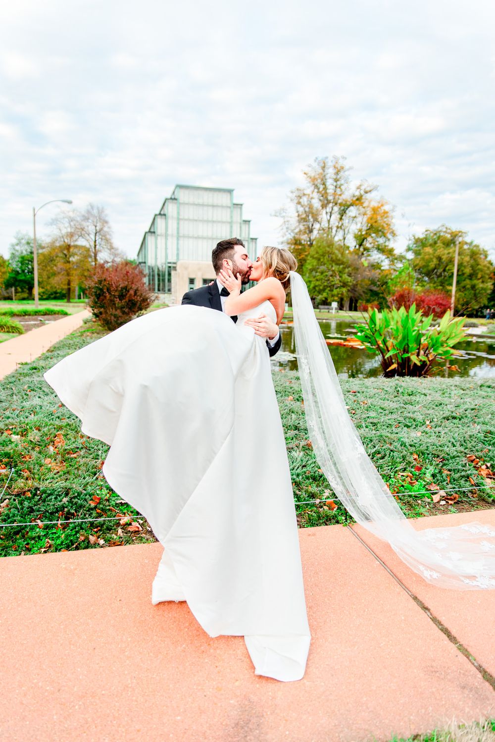 groom carrying bride in his arms and smiling at each other at the Jewel Box in Forest Park, STL