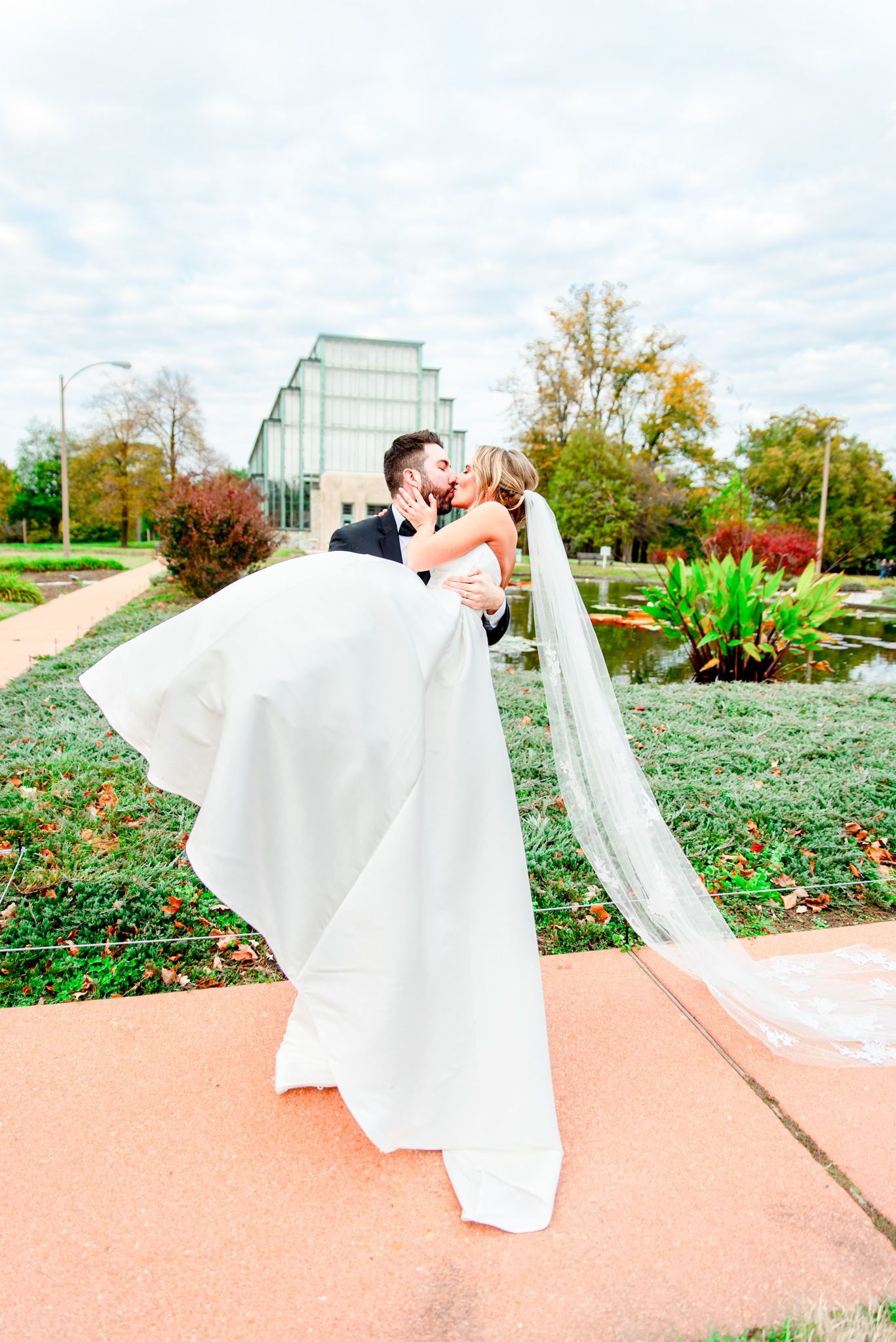 groom carrying bride in his arms and smiling at each other at the Jewel Box in Forest Park, STL