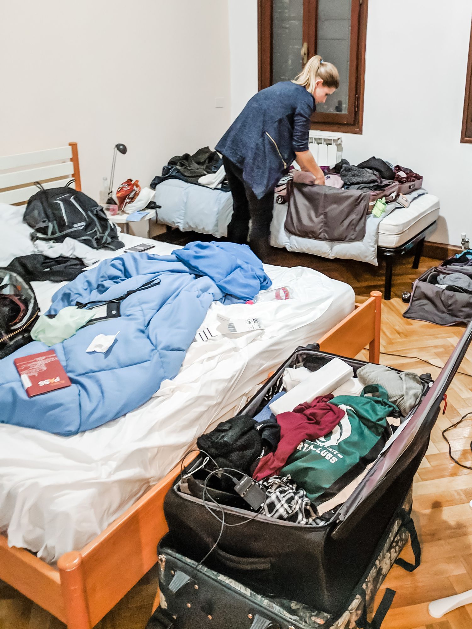 Girl packing a suitcase in a very messy bedroom with clothes everywhere