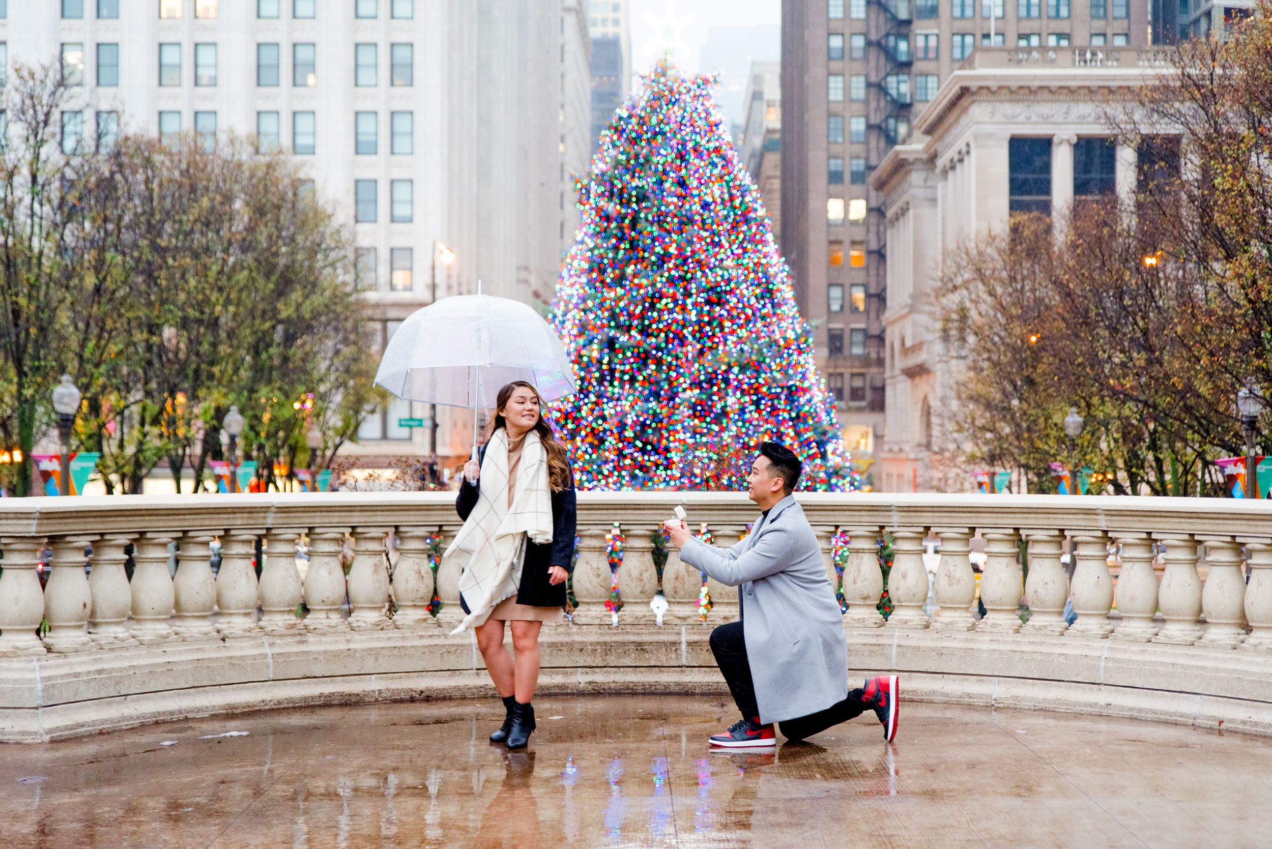 Man in gray coat kneeling down in front of Christmas Tree at Millennium Park in Chicago about to propose