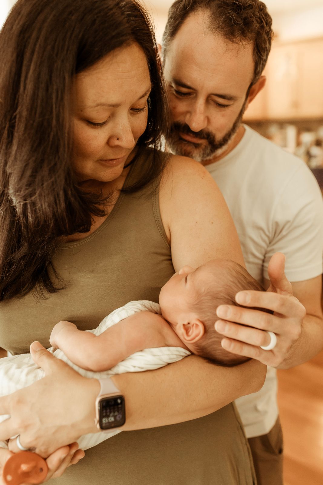 Mother and father gaze down at their newborn during a photography session in their home in Longmont, Colorado