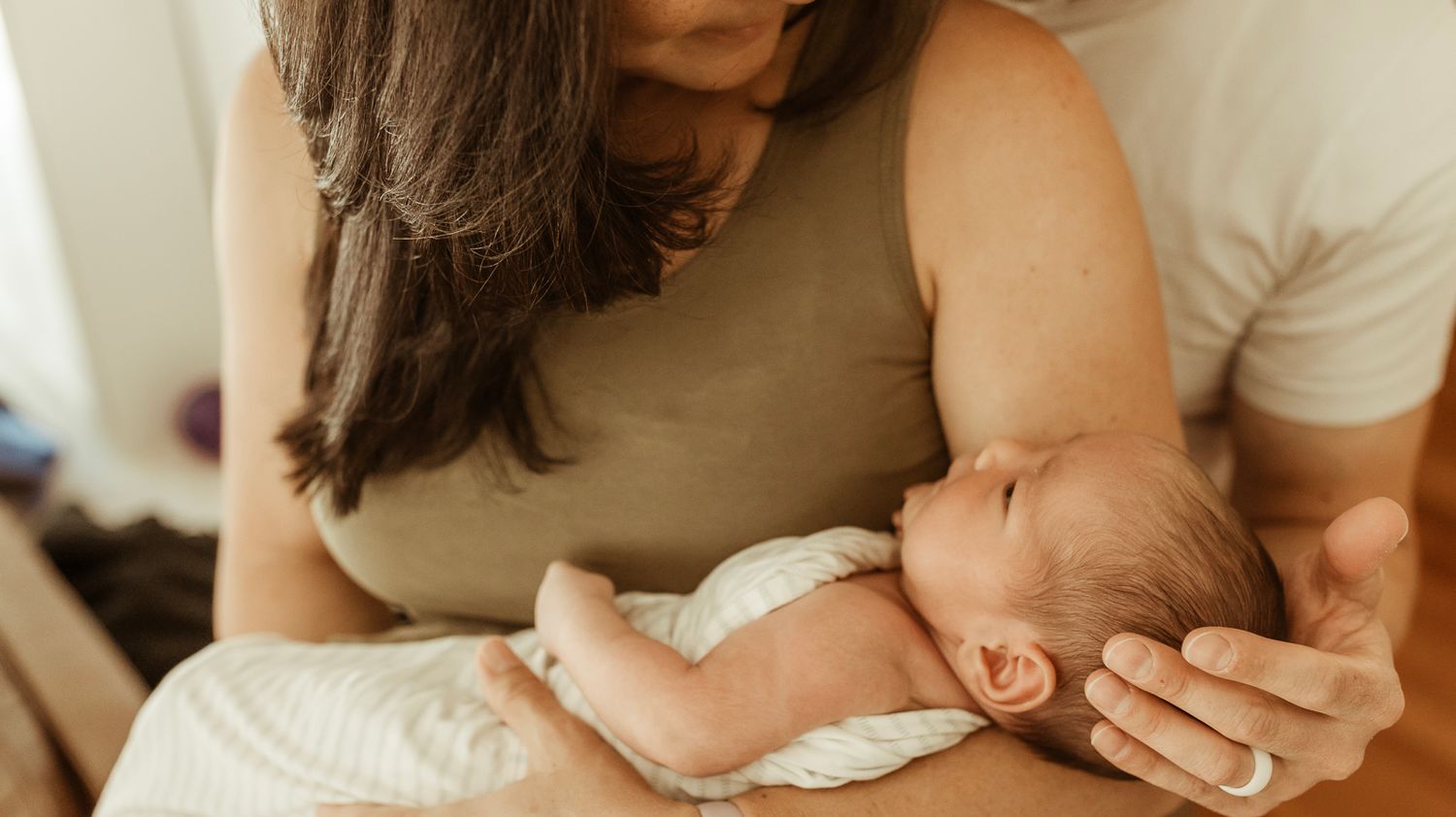 Mother holds her newborn and father rests his hand on the baby's head during their newborn photography session in CO