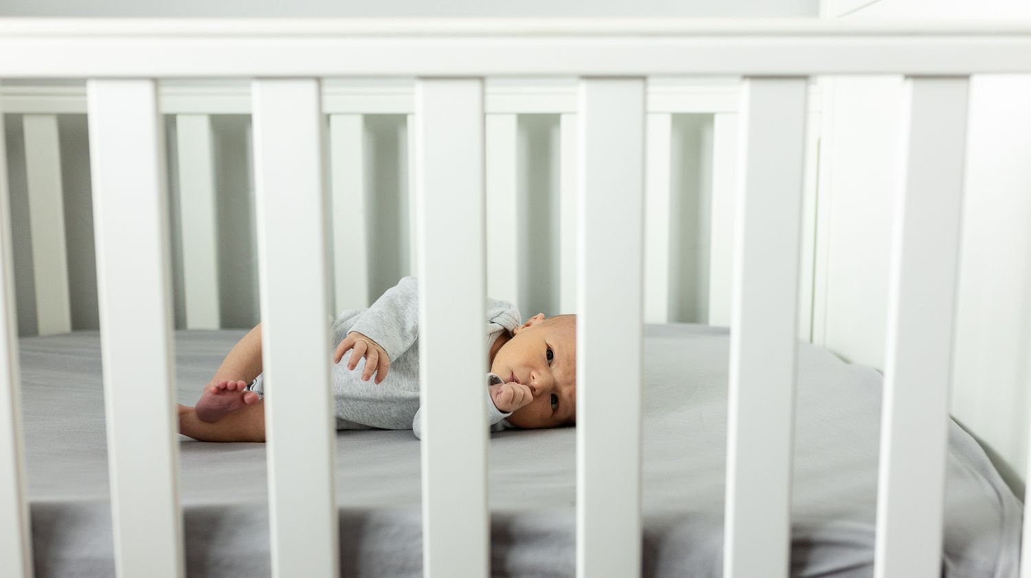 Newborn baby as seen through the slats of his crib during his lifestyle newborn photography session in Longmont, CO