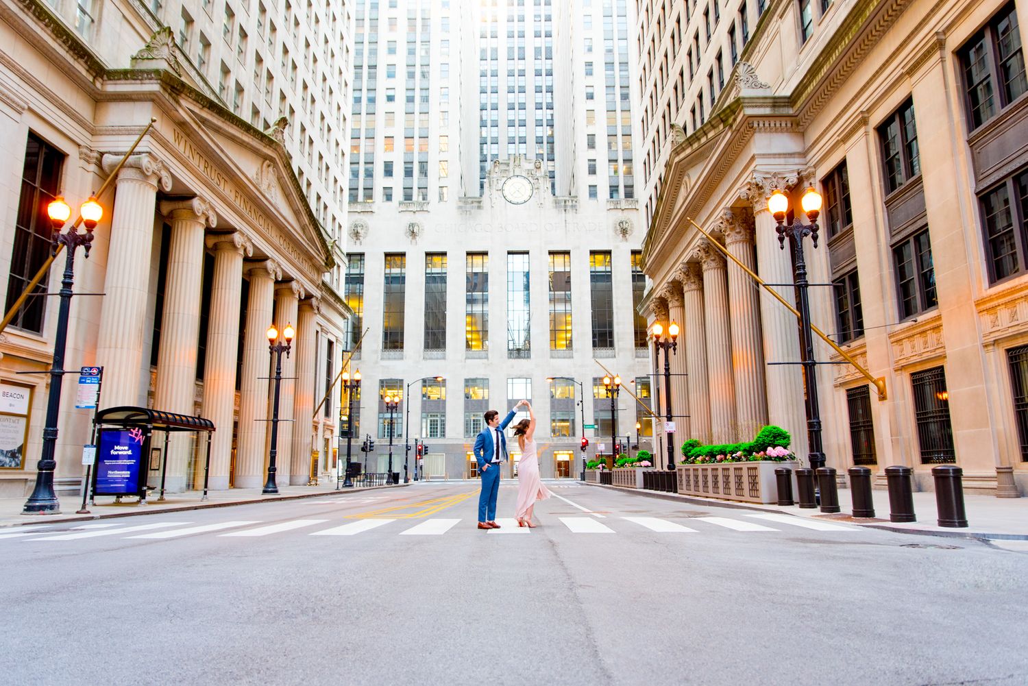man in navy suit spins woman around in front of Chicago Board of Trade in empty street at sunset