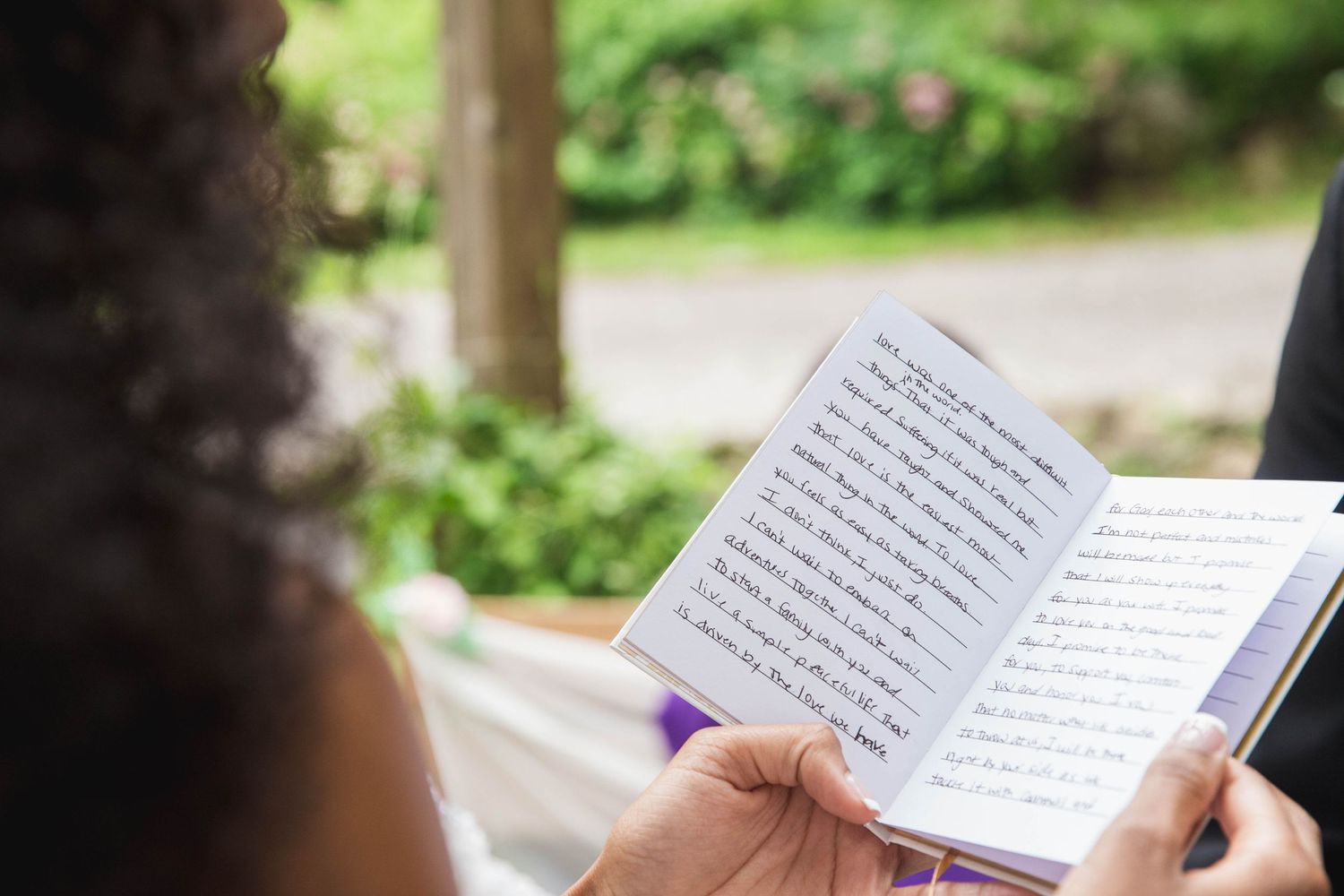 Close-up shot of hands holding an open wedding ceremony book with handwritten text.