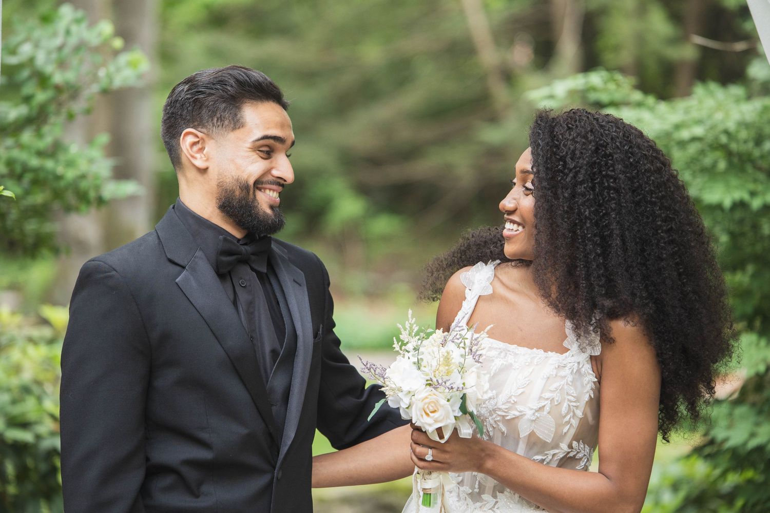 A candid moment of joy and laughter shared between a wedding couple in a garden setting.