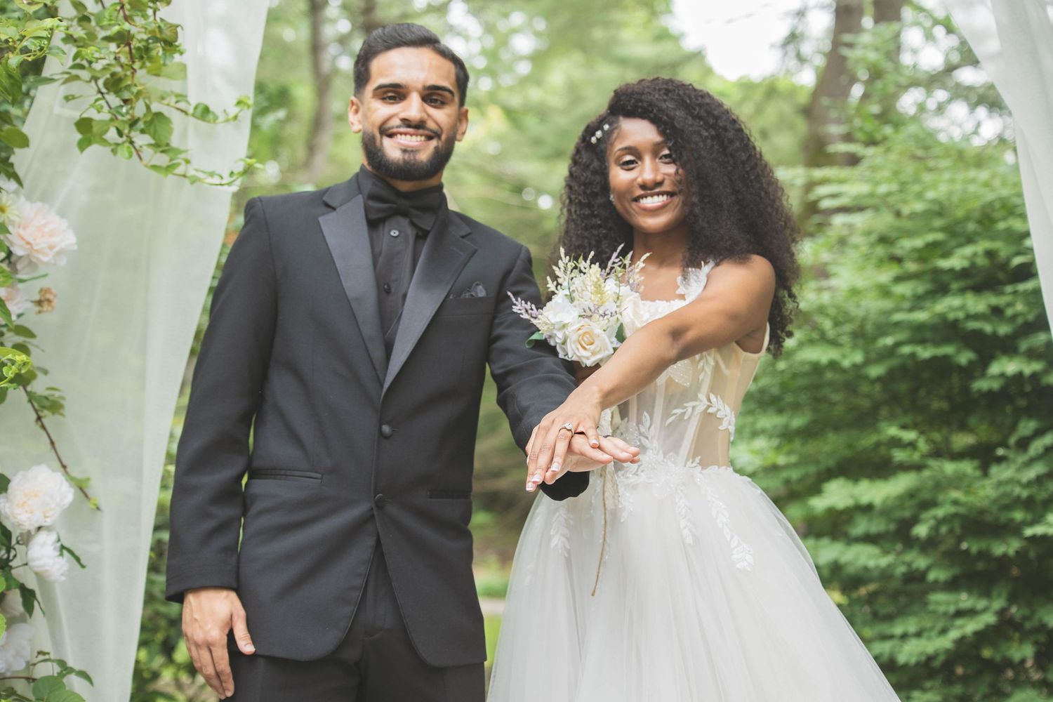 A romantic wedding portrait of a couple standing together against a backdrop of green foliage.