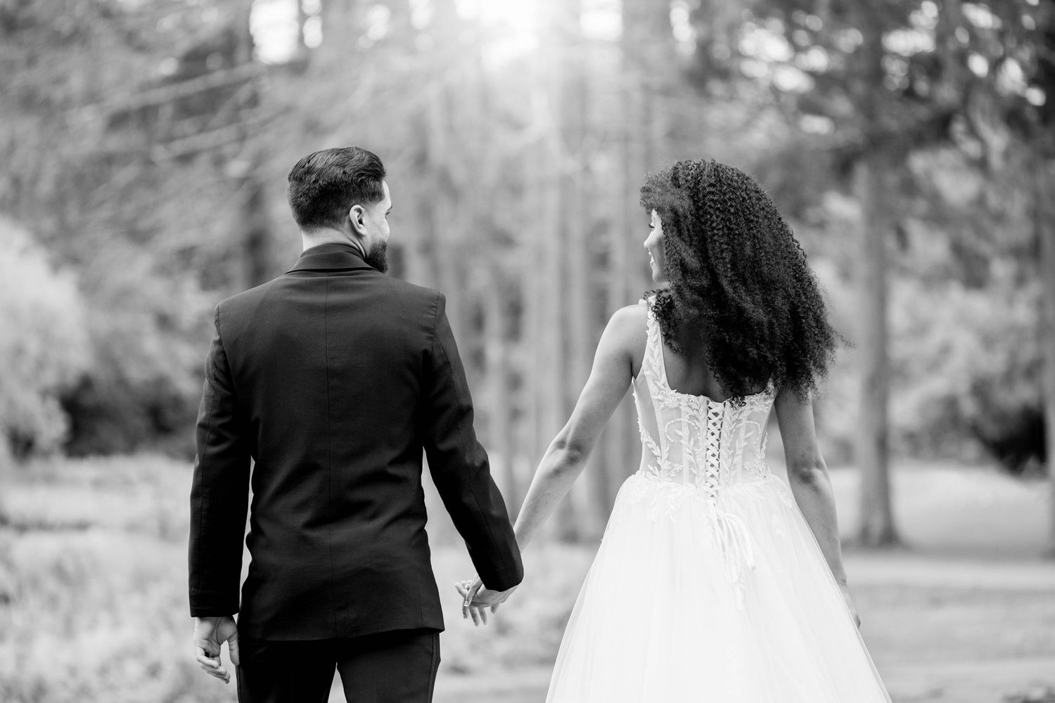 A black and white romantic portrait of newlyweds walking together in a wooded setting.