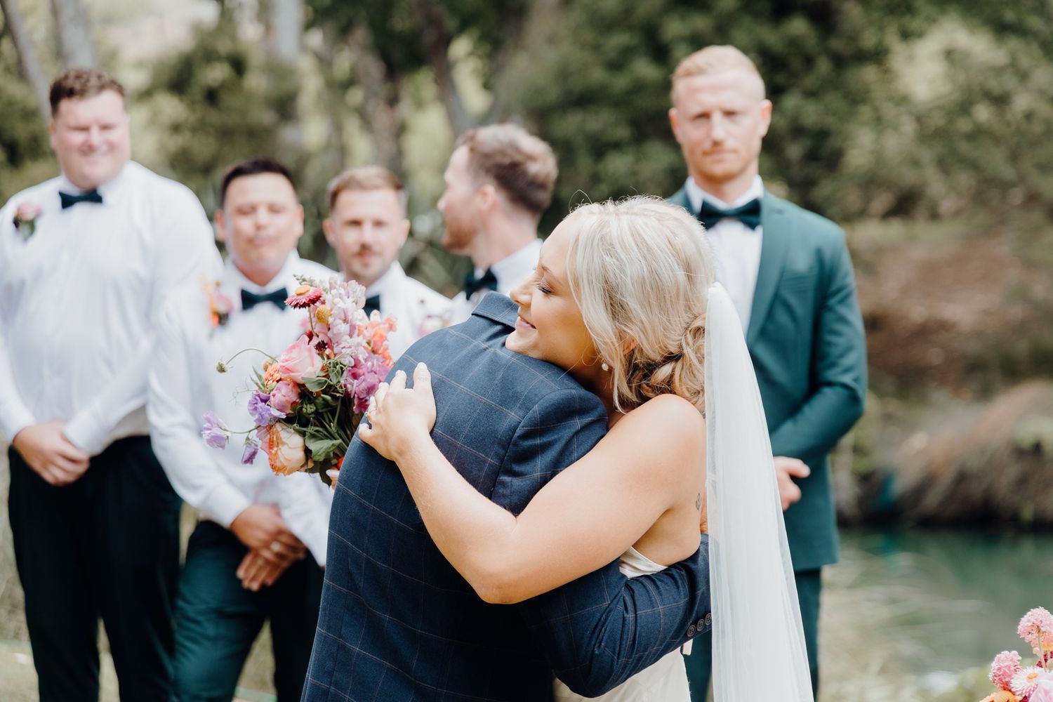 Wedding party gathers outdoors for emotional moment during ceremony.