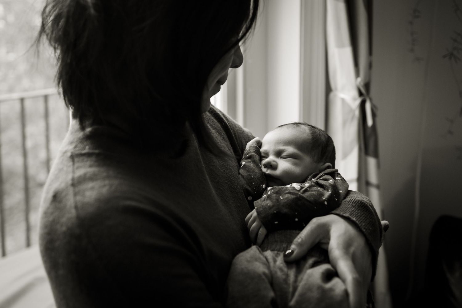 Newborn photography in Hampstead home. Newborn baby being held beside a window.