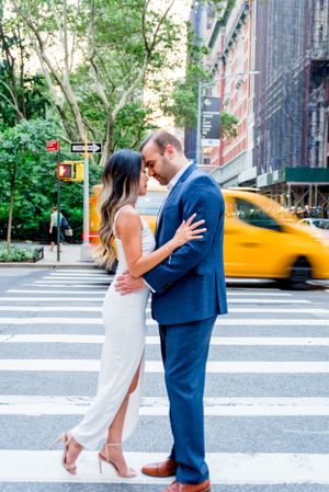 man and woman putting forehead together hugging as yellow taxi drives behind them in Madison Square Park