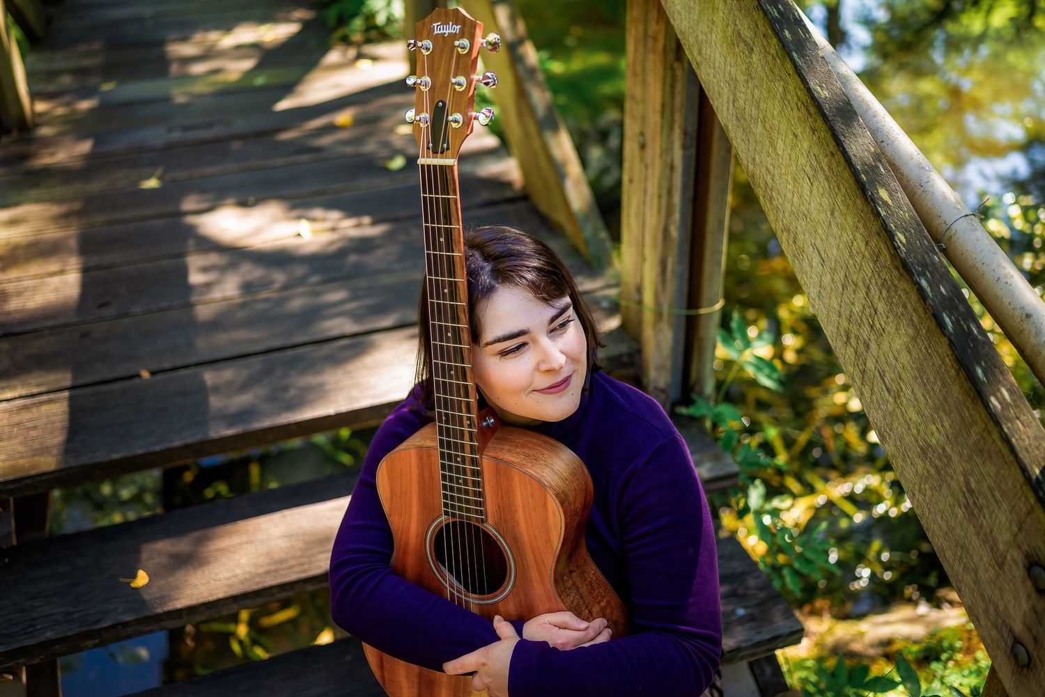 Female singer in purple jumper hugging her acoustic guitar.