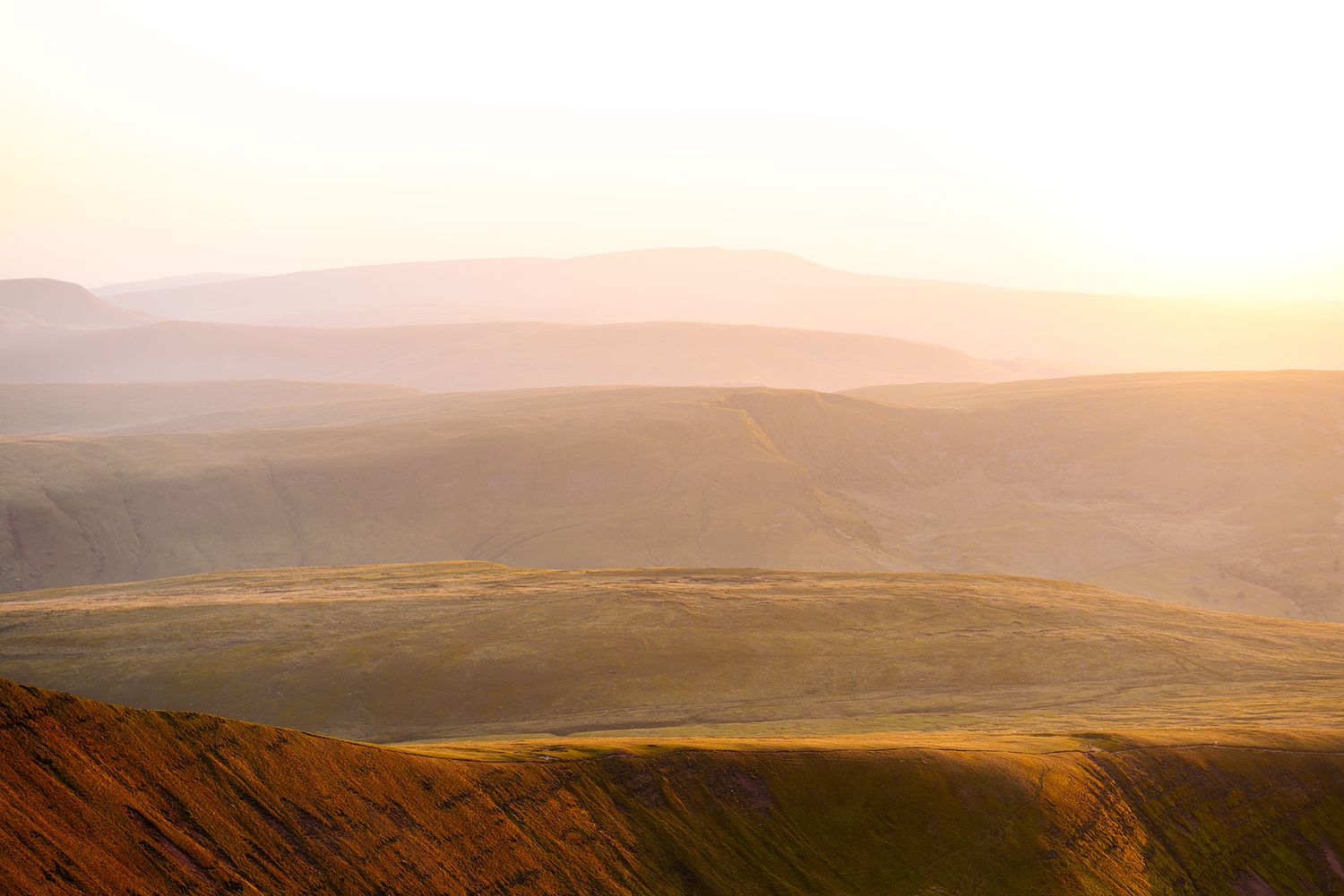 Golden sunlight illuminates misty rolling hills during a scenic mountain sunset.