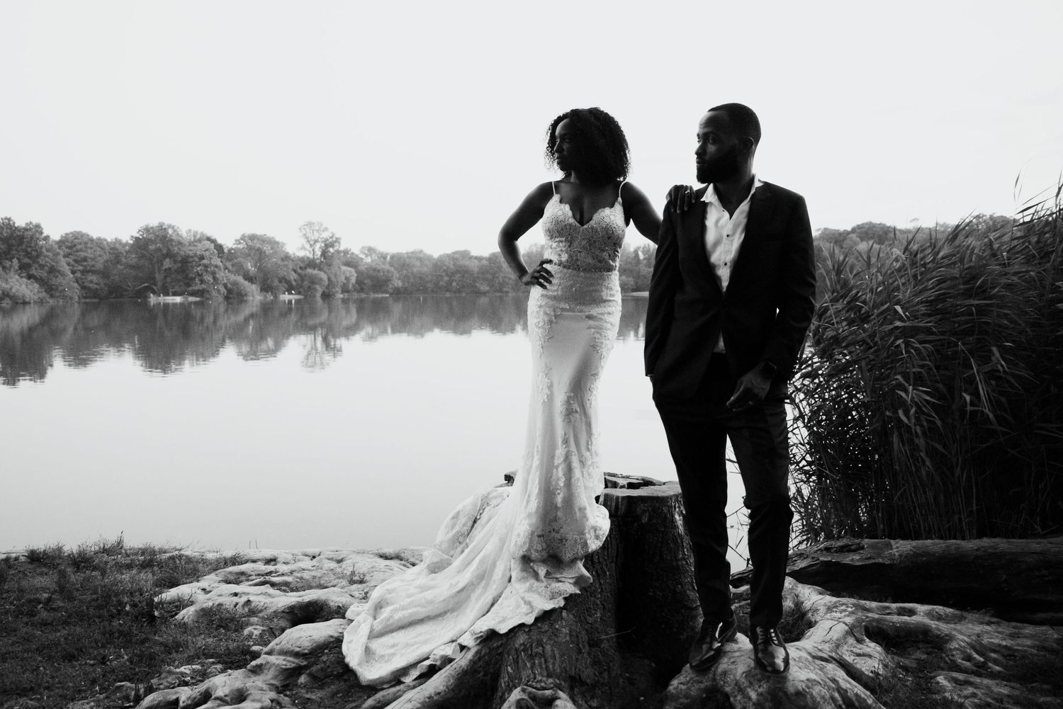 A dramatic black and white wedding photo by a serene lake with a flowing dress.