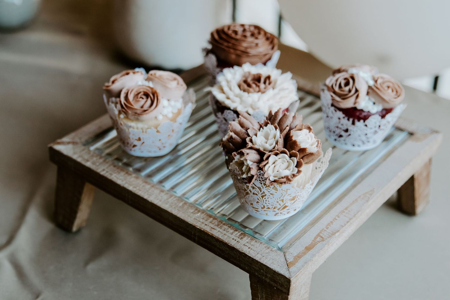 Delicate rose-colored cupcakes with floral decorations displayed on rustic wooden tray.