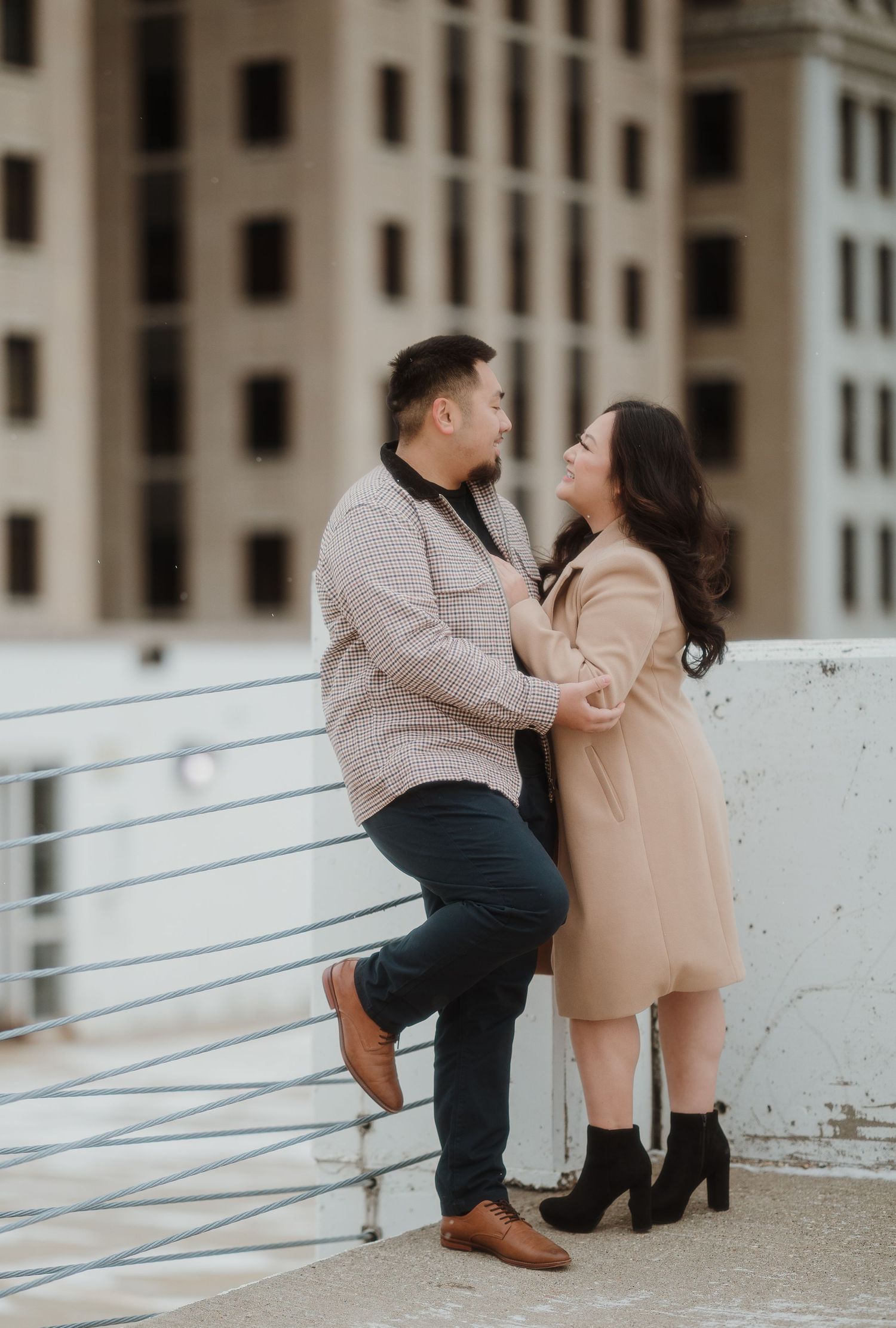A playful couple sharing an intimate moment against an urban backdrop with concrete buildings.