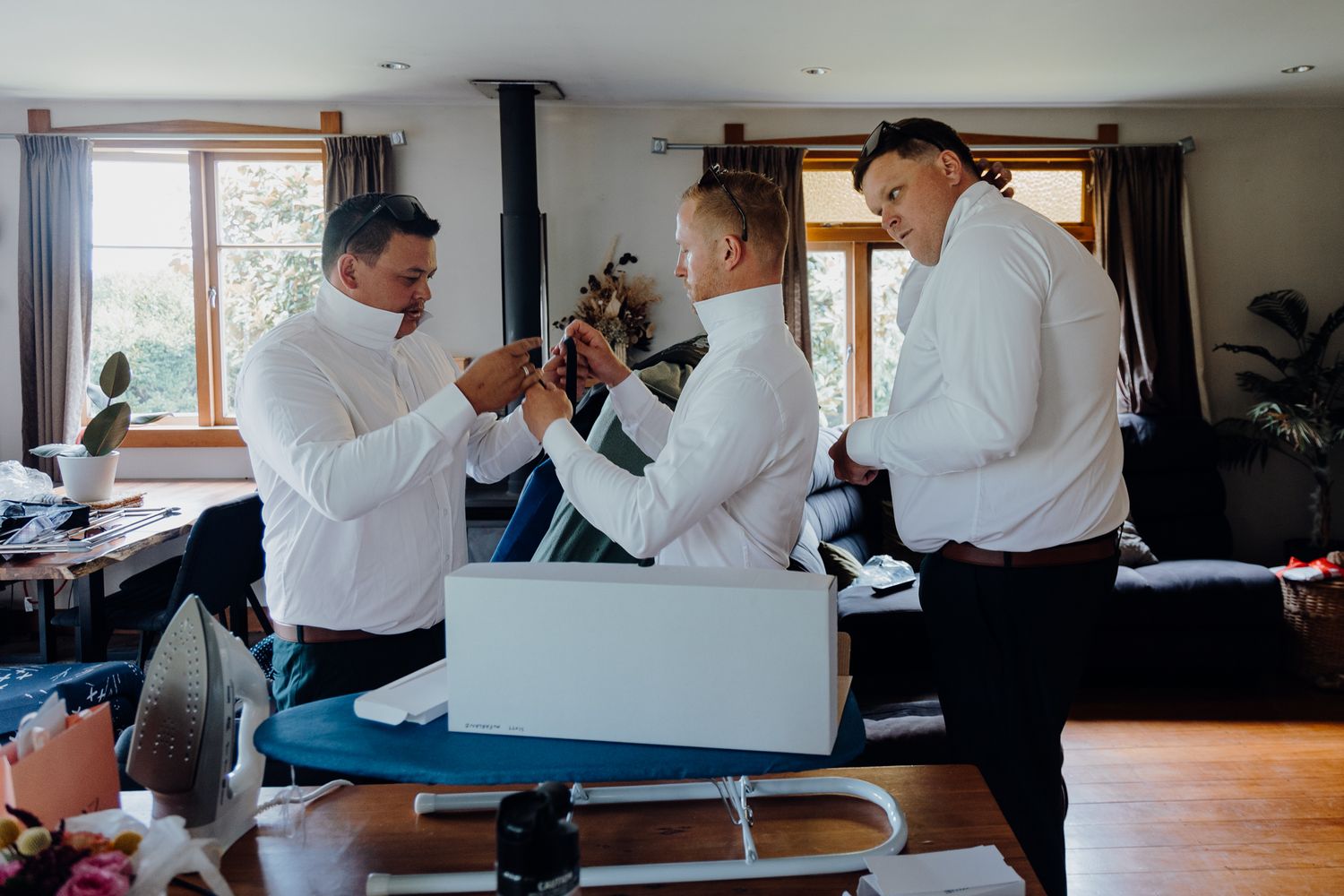 Three people in white dress shirts interact playfully in a living room setting.
