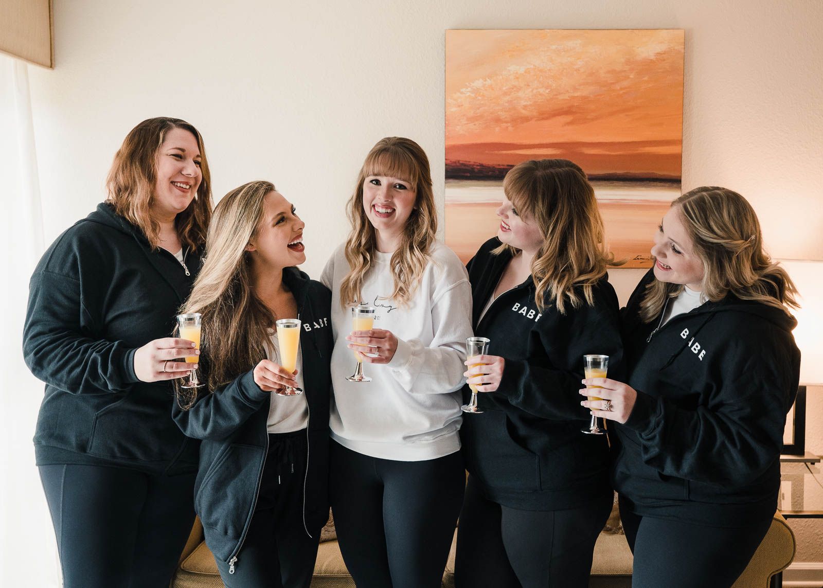 Bride and her bridesmaids having mimosas together in their custom sweatshirts