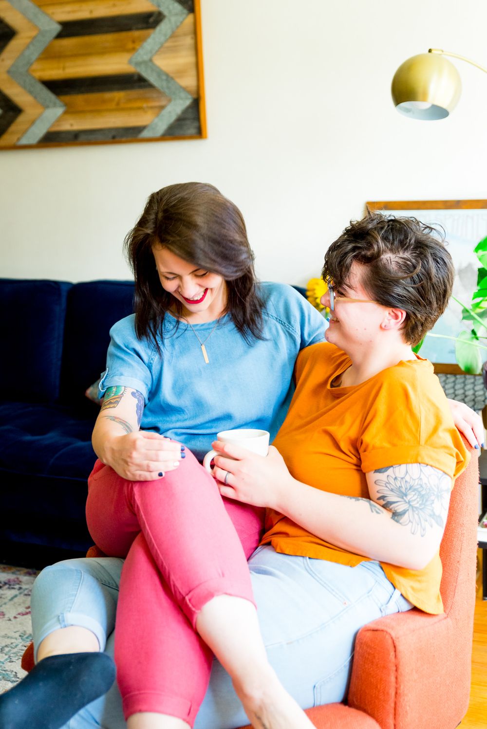 woman in blue shirt and pink pants laughing with her wife in orange shirt