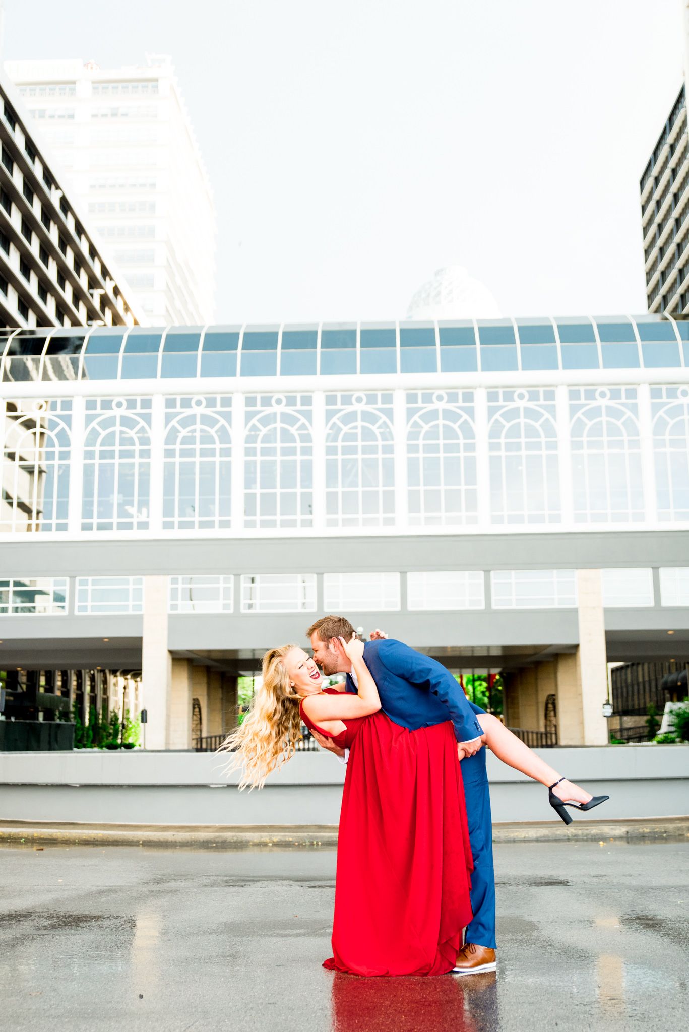 man in navy suit dipping woman in red dress with blonde hair and she laughs