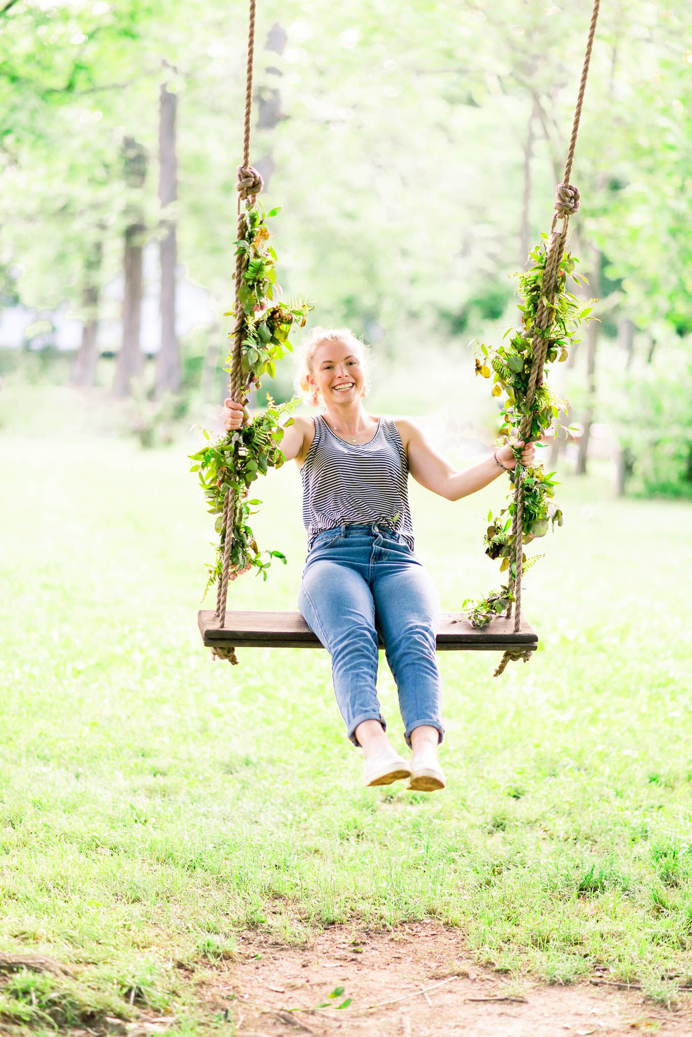 jeans and tank top young lady swinging on floral rope swing outside