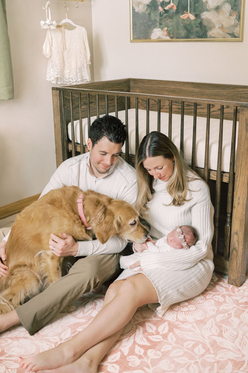 Family and golden retriever share intimate moment with newborn by wooden crib.