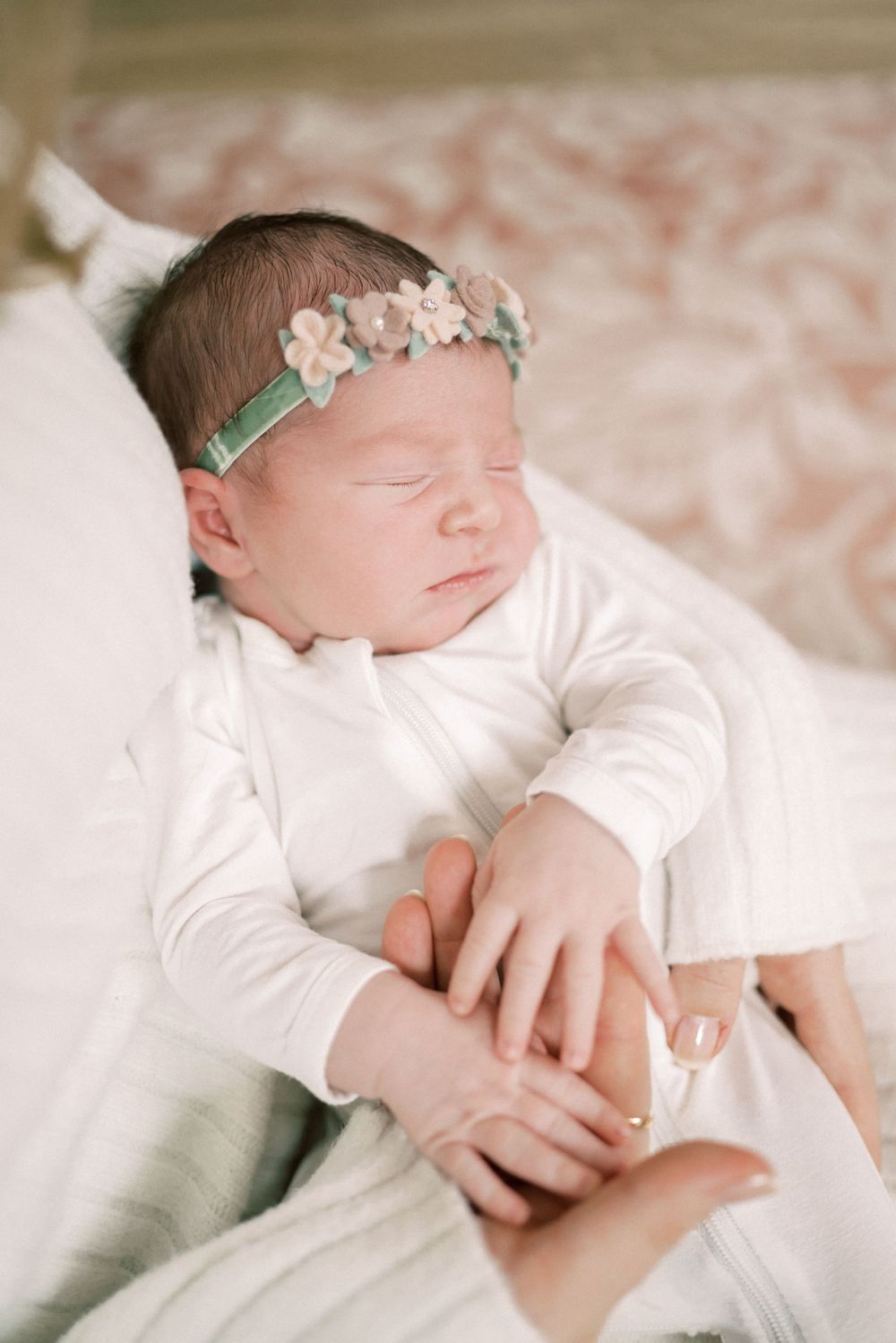 Peaceful sleeping newborn wearing white clothing and floral headband.