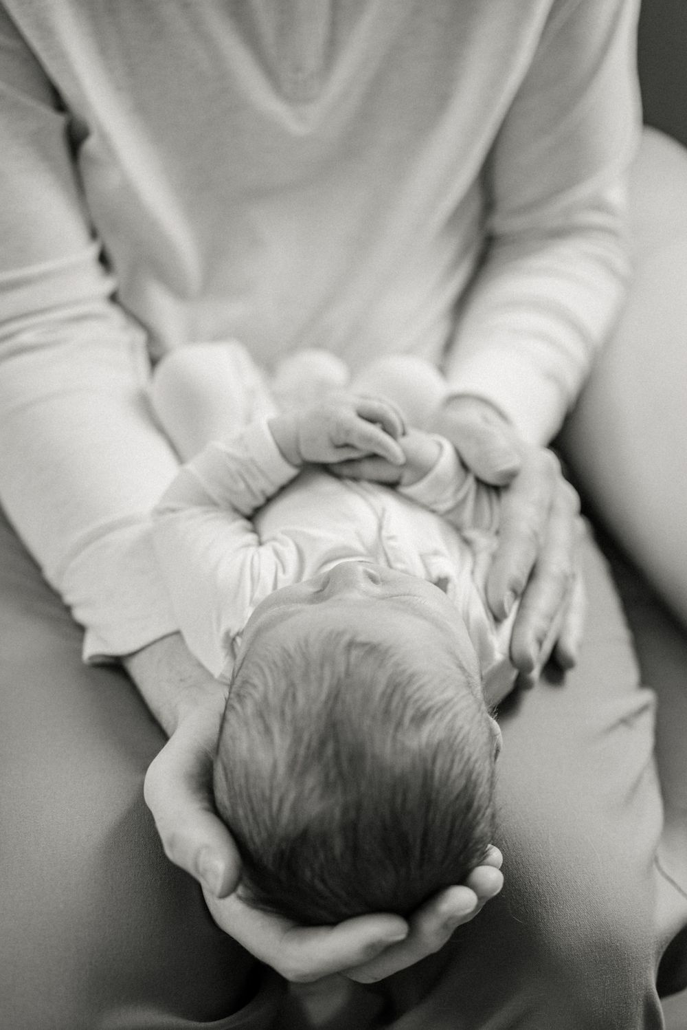 Black and white portrait of gentle hands cradling sleeping newborn.