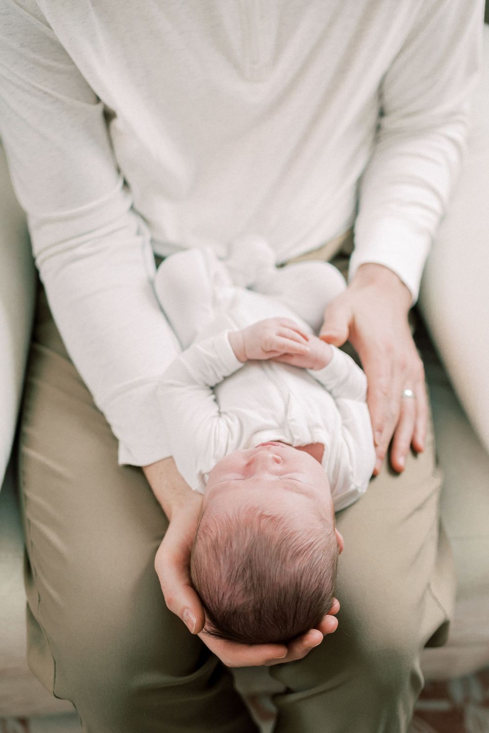 Overhead view of sleeping newborn in white being cradled.
