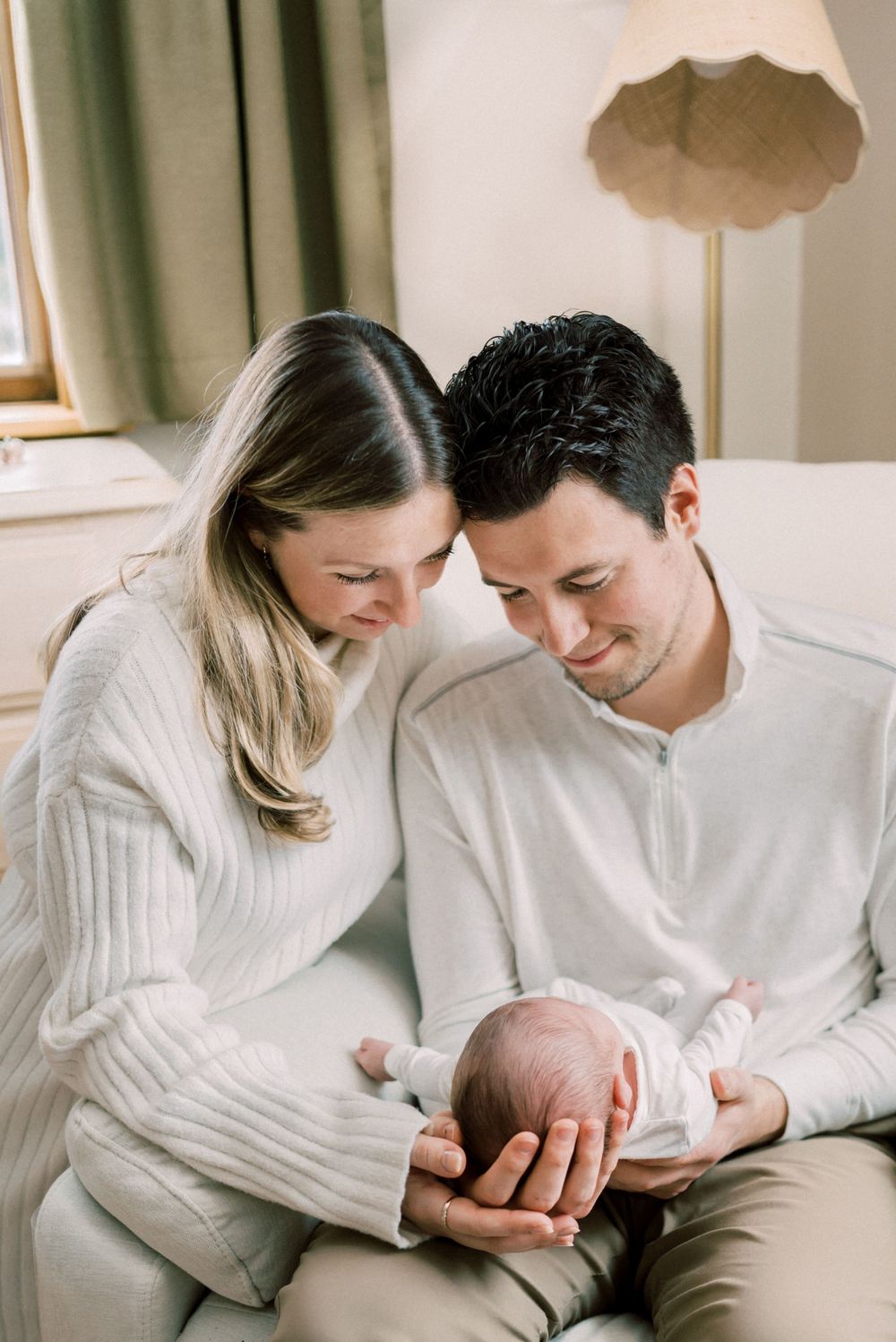 Parents in white sweaters sharing intimate moment with their newborn in cozy room setting.