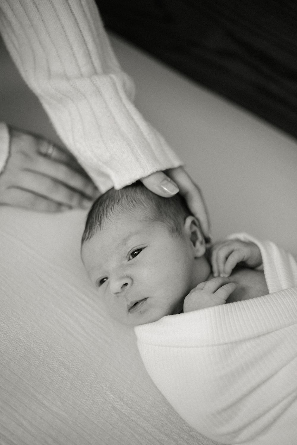 Black and white portrait of alert newborn swaddled in white fabric.