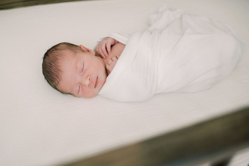 Peaceful newborn wrapped in soft white blanket sleeping on white surface.