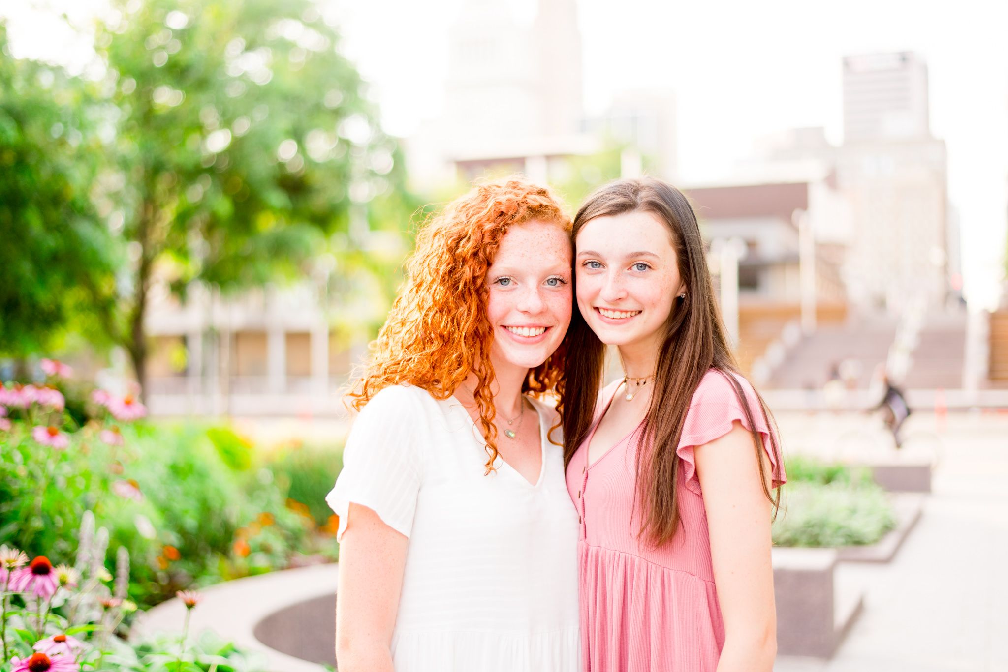 two teenage girls with red hair and brown hair stand together smiling in Smale Park at sunset