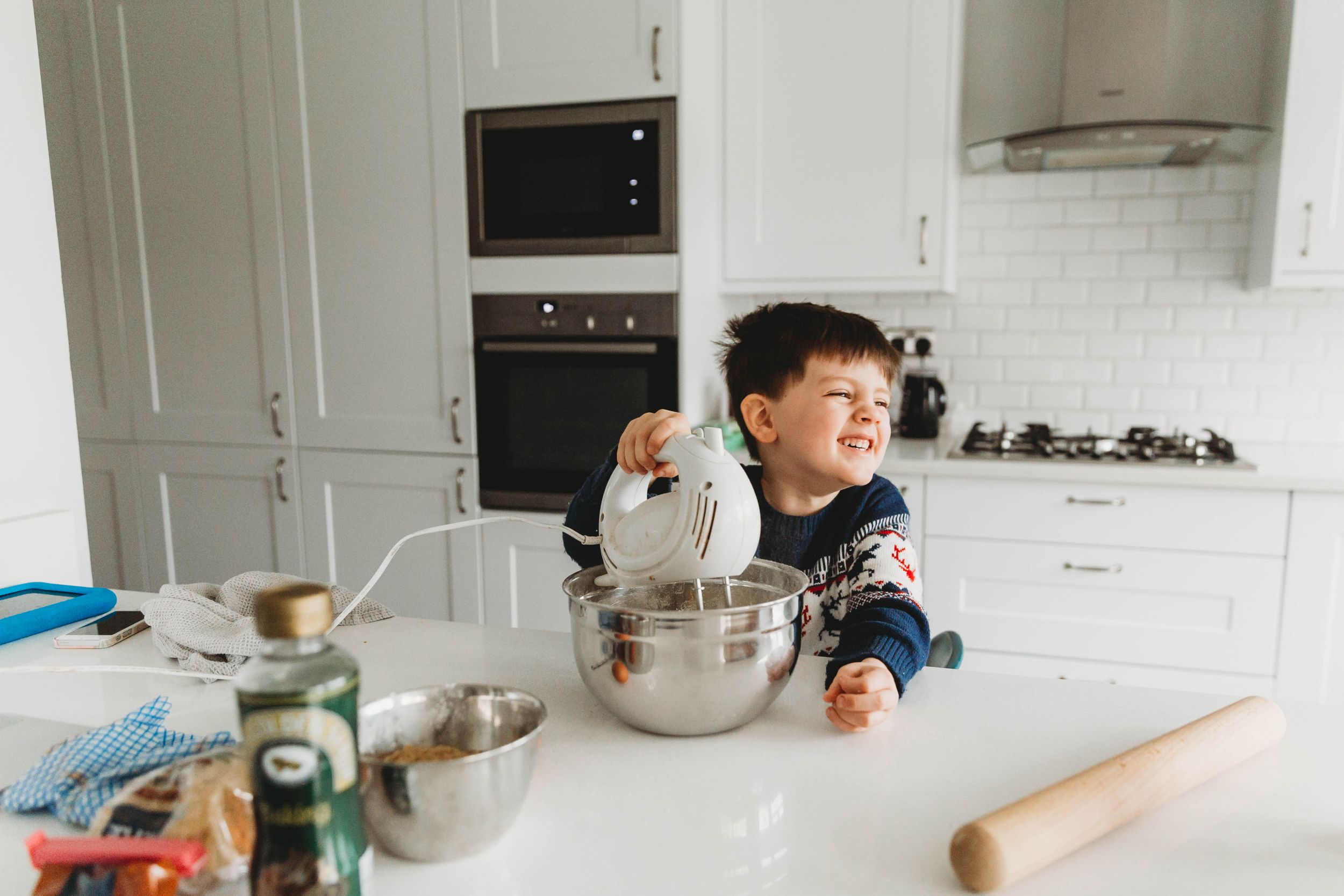 little boy in navy sweater mixing cookie dough with a handheld mixer