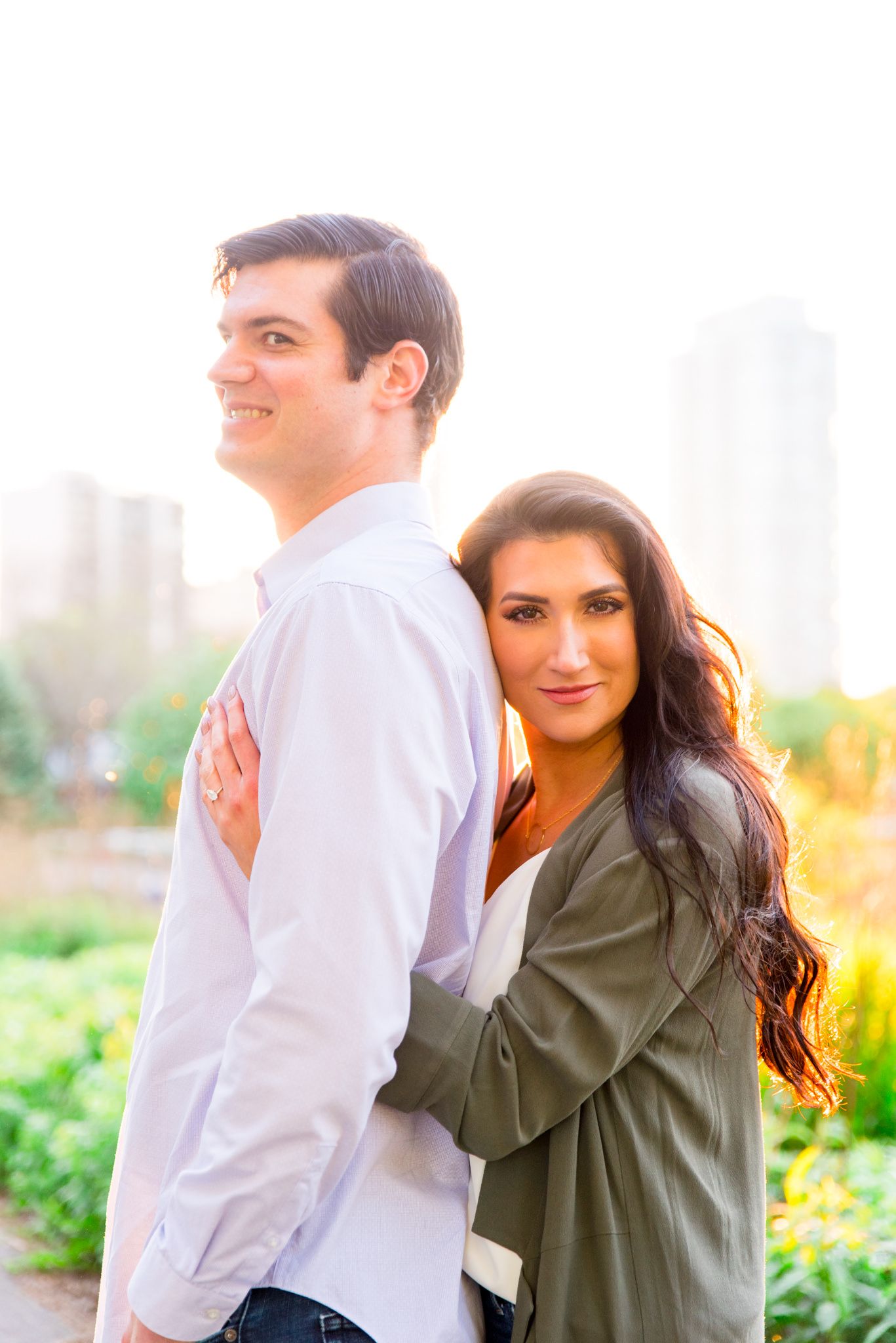 woman with long dark hair hugging fiance from behind and looking into the camera