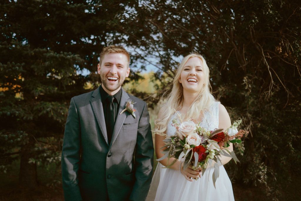 Wedding couple poses in forest with autumn foliage and natural lighting.