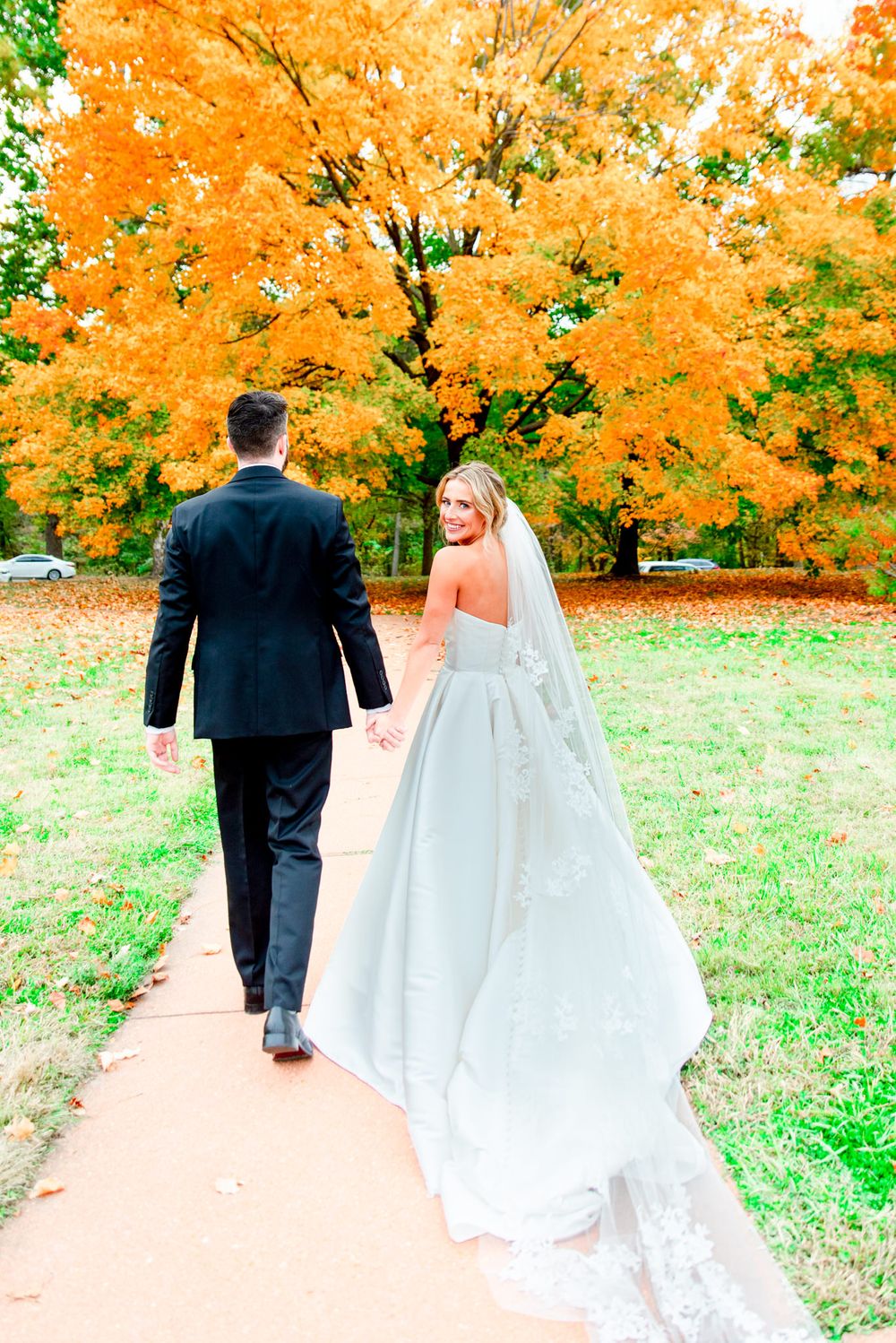 bride and groom walk away holding hands, bride looking back