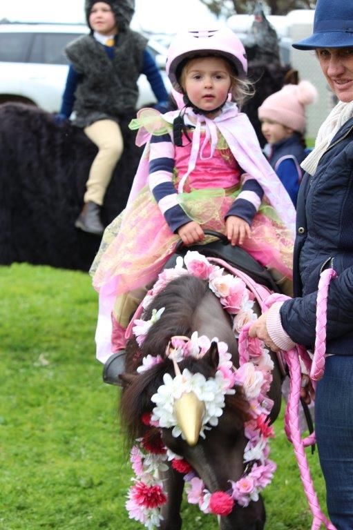 Young equestrian on decorated pony wearing pink riding attire at outdoor event.