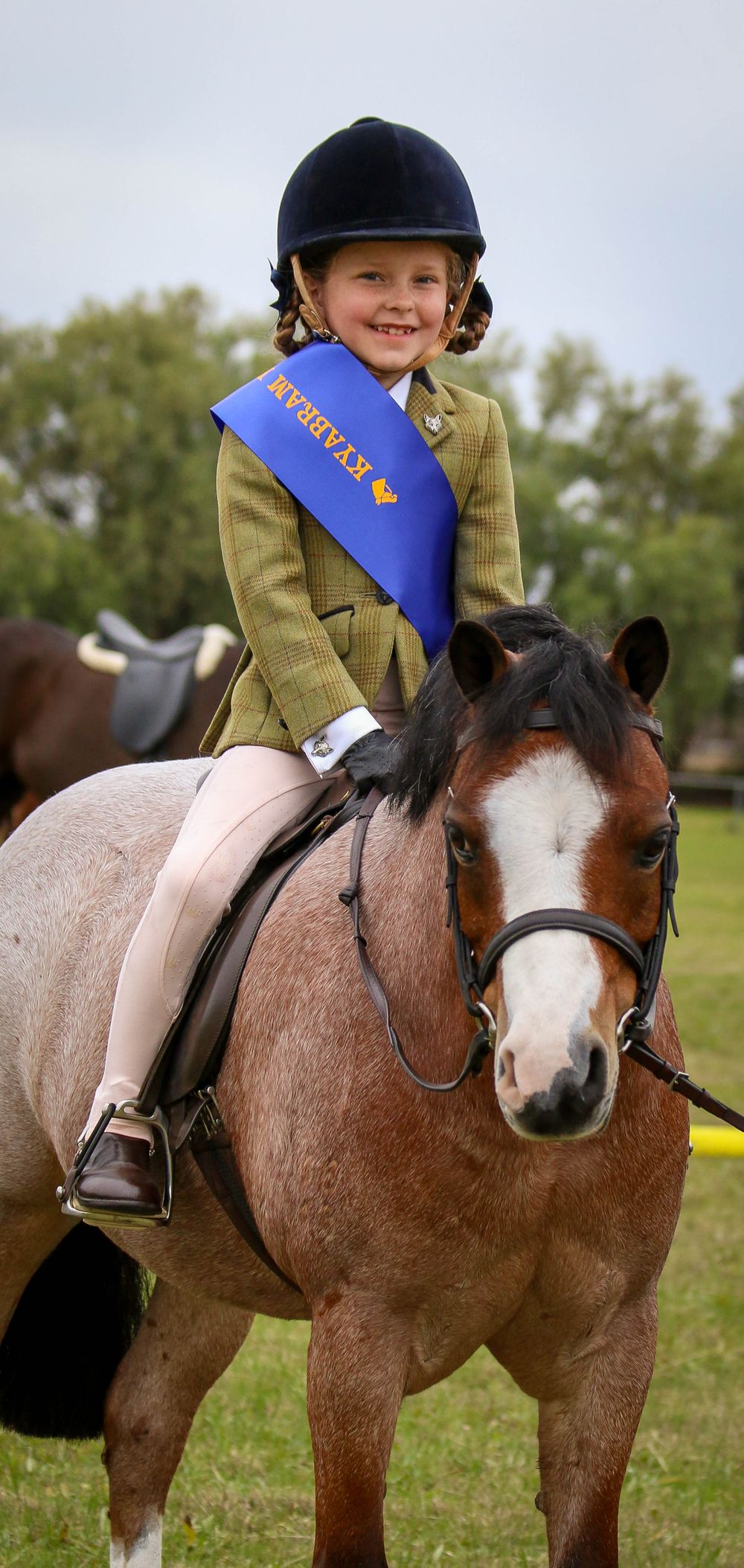 Young equestrian in formal attire riding a brown and white pony.