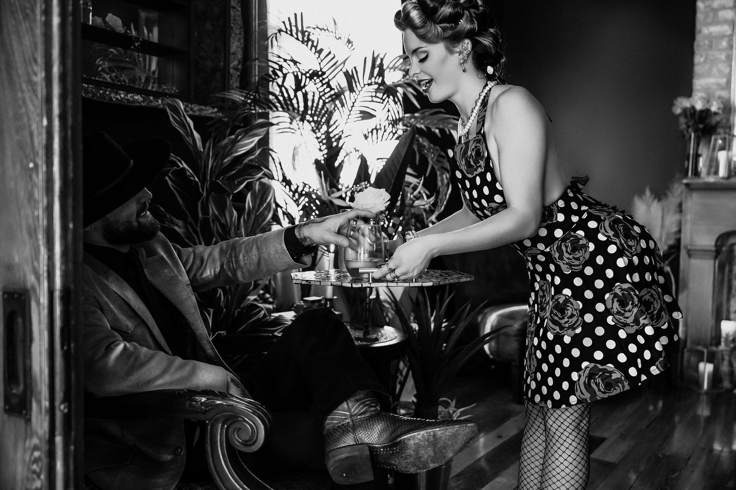 Vintage style black and white photo of person serving drinks in polka dot dress.