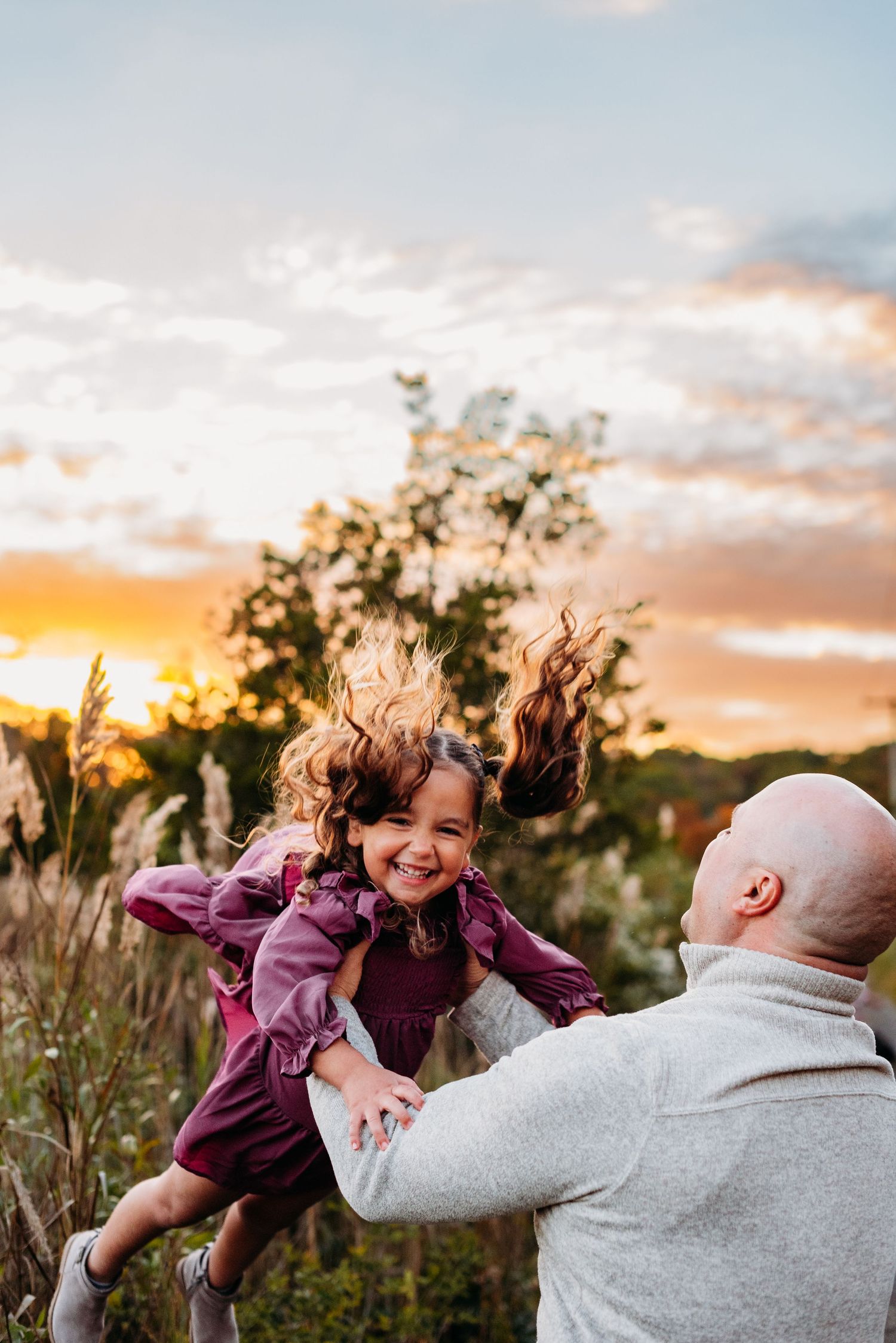 Joyful playtime outdoors at sunset in a field of tall grass with hair blowing in the wind.