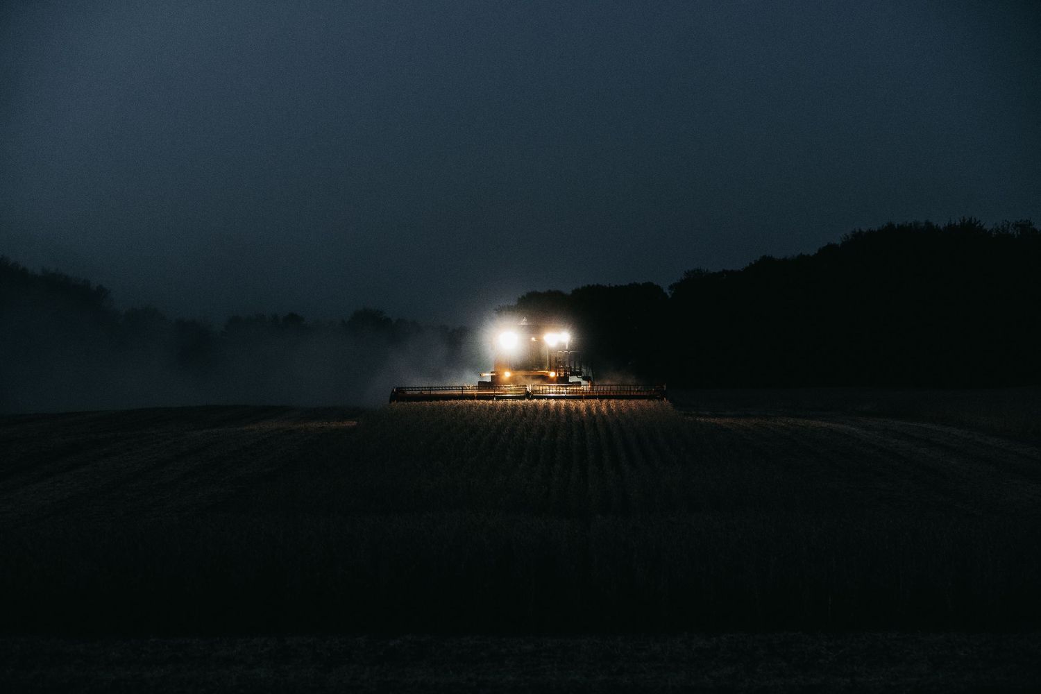 Farm machinery with bright headlights harvesting crops during nighttime operation.